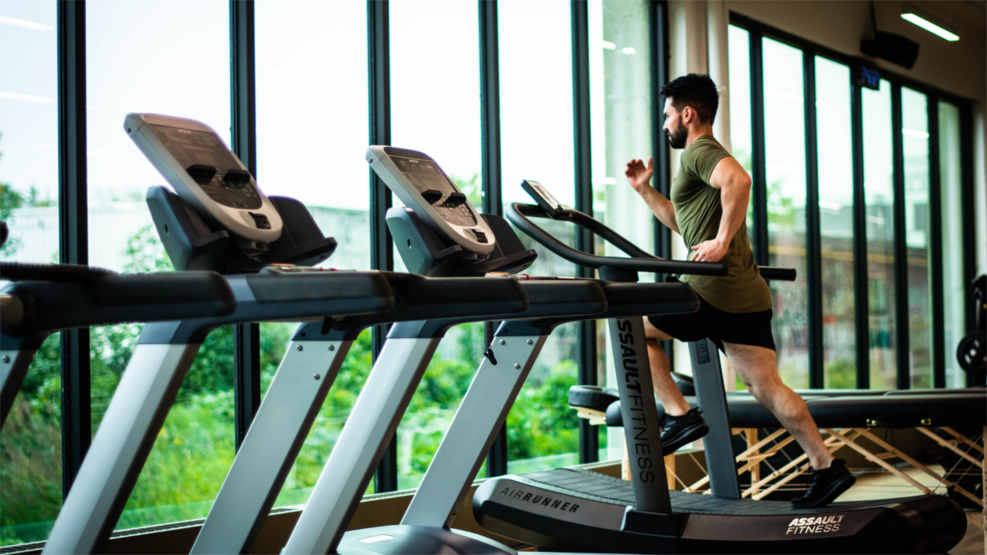 A man in black shorts and green t-shirt exercises on a treadmill